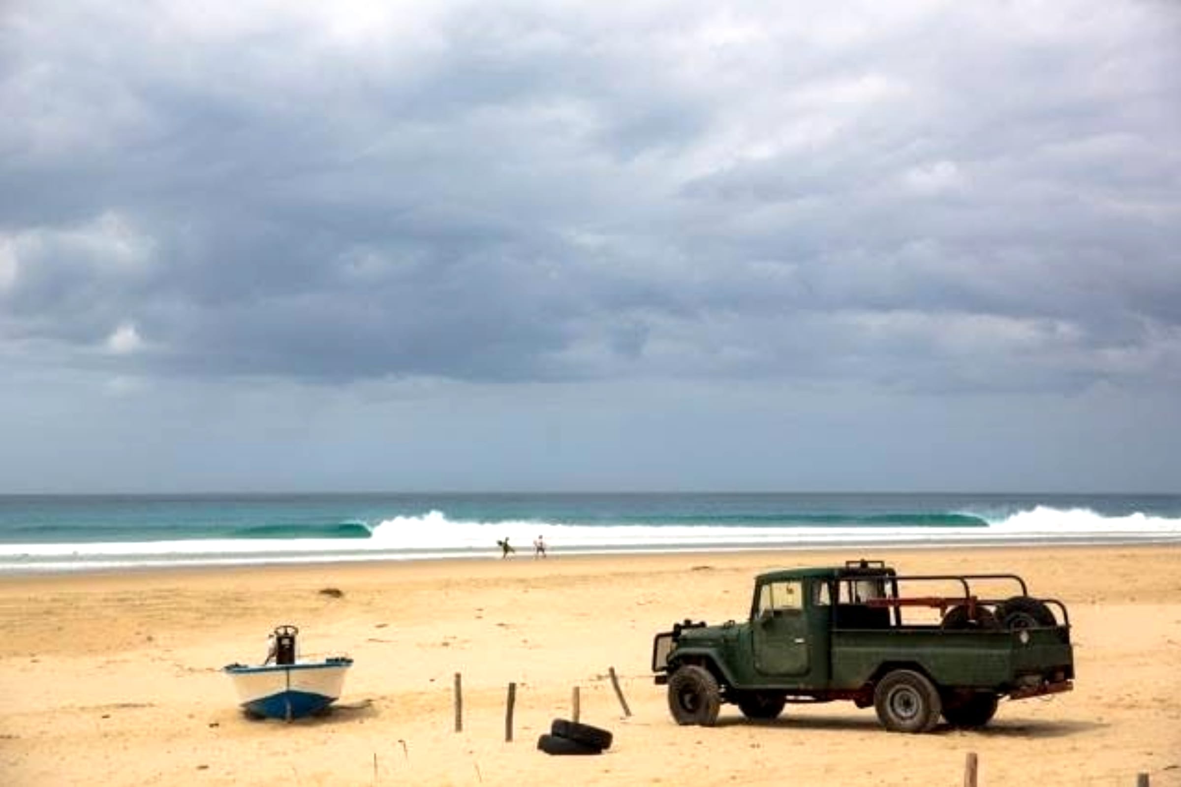 Land Cruiser and a fishing boat on an empty Mozambique beach, a wave peeling behind