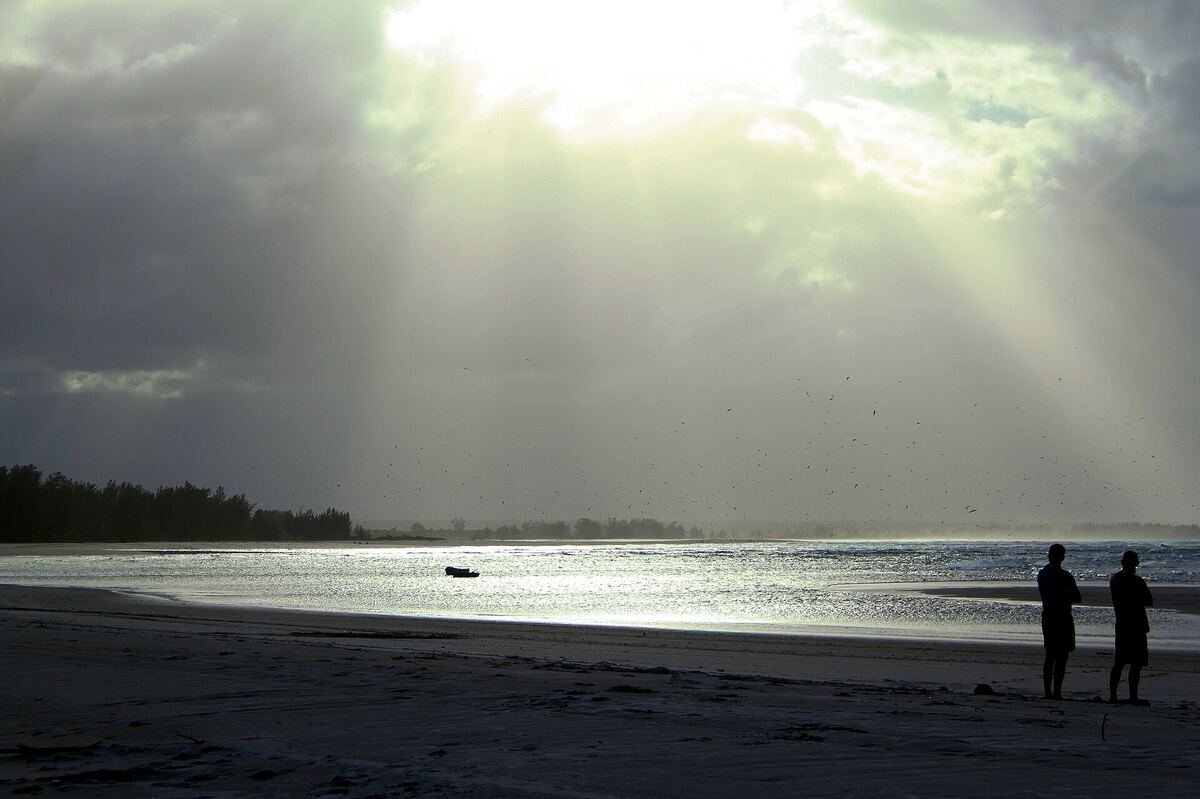 Two people on the shore of the Pomene estuary as light breaks through cloud