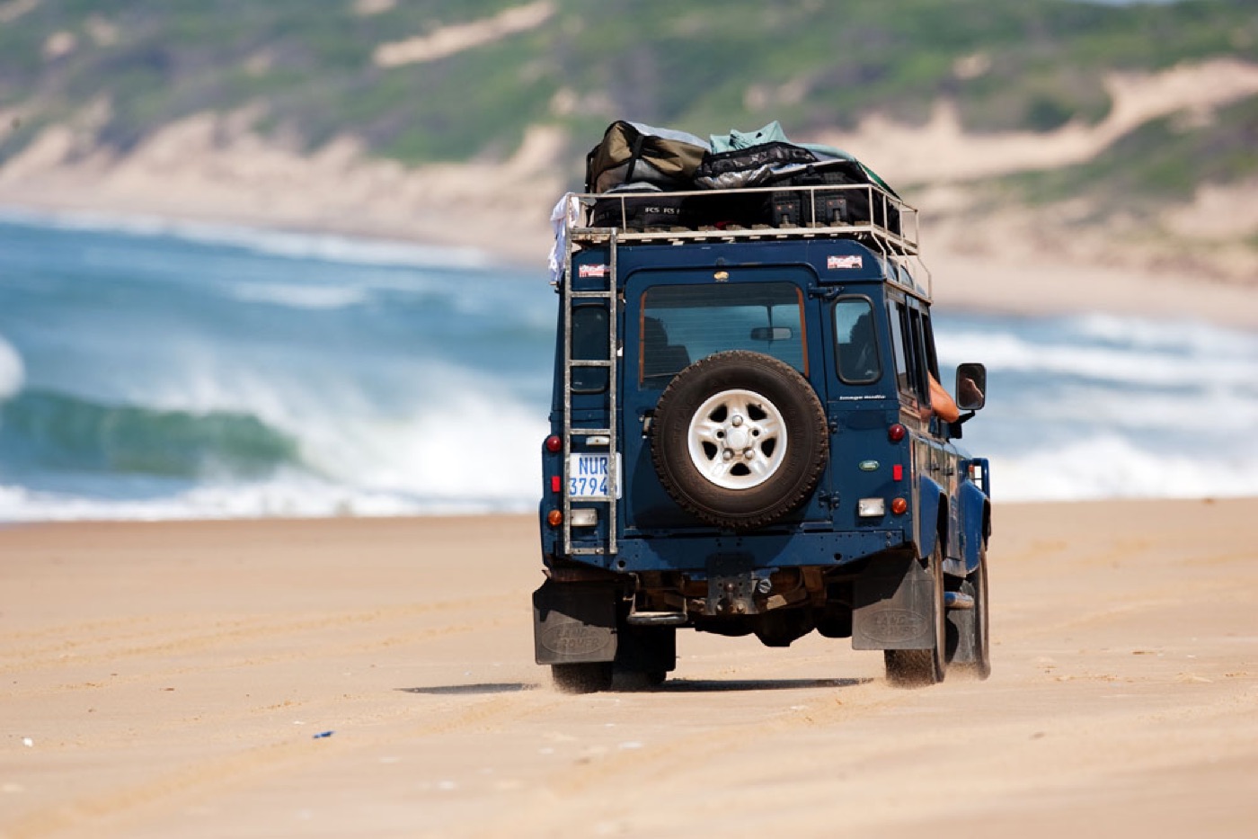 Land Rover with boards on the roof driving along the beach